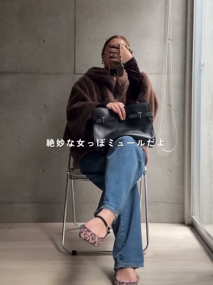 ブラウンのファーコートとデニムにレオパードのストラップミュールを合わせて椅子に座ったところ