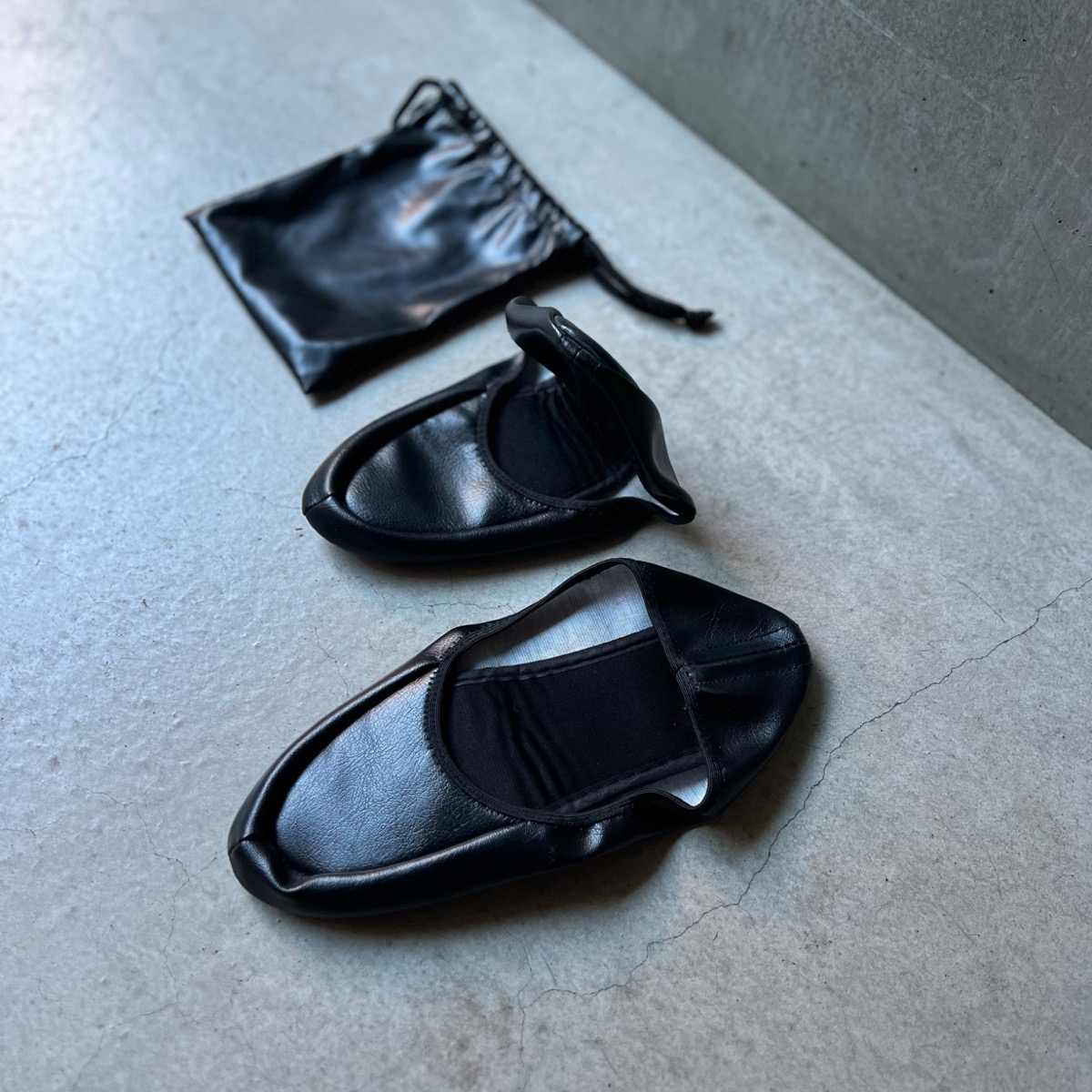 1,240円の折りたたみシューズ（黒）。片方を折りたたんだところと、付属のレザー調の巾着